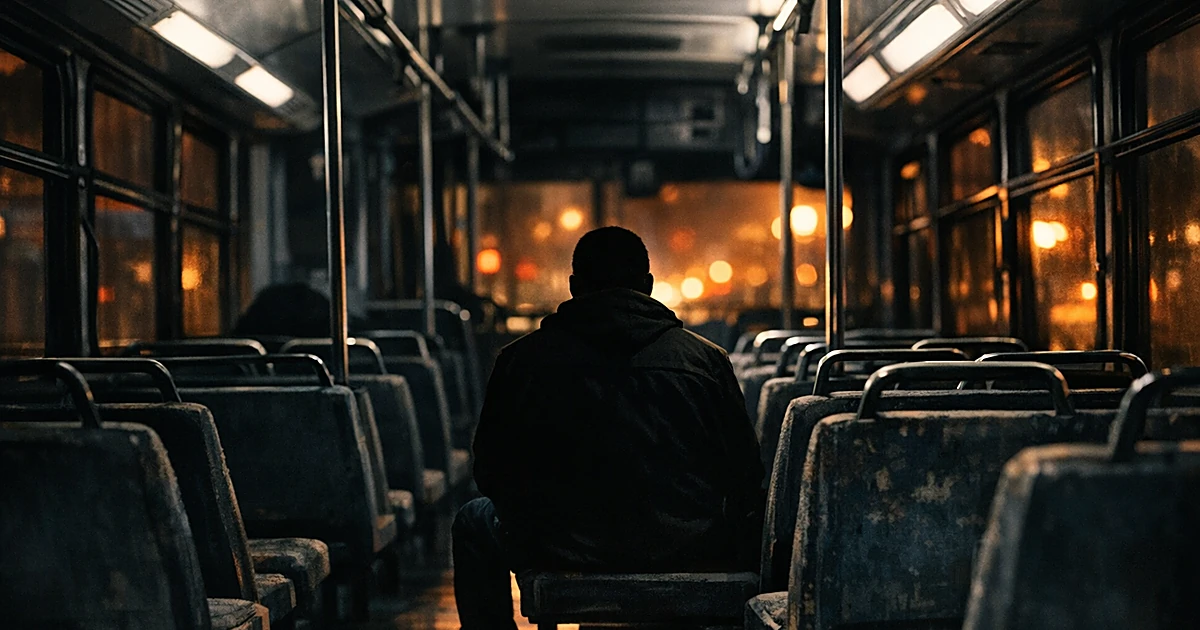 Dark interior of a public bus with silhouetted passenger sitting alone among empty seats in dim lighting