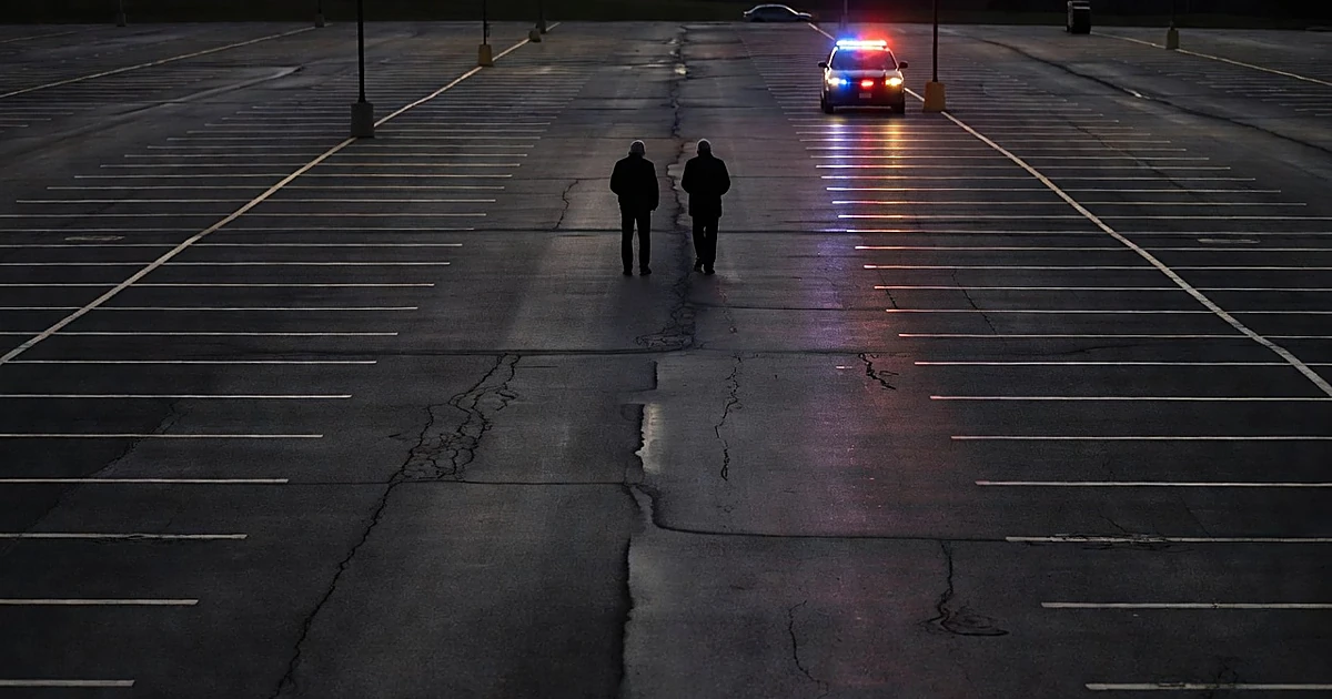 Empty sports complex parking lot at dusk with elderly silhouettes and police vehicle with emergency lights